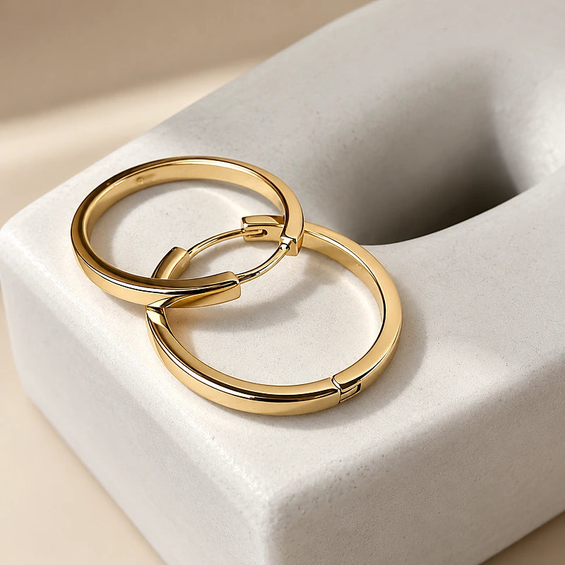 Boucles d'oreilles créoles Manon, la paire dorée posée sur du marbre