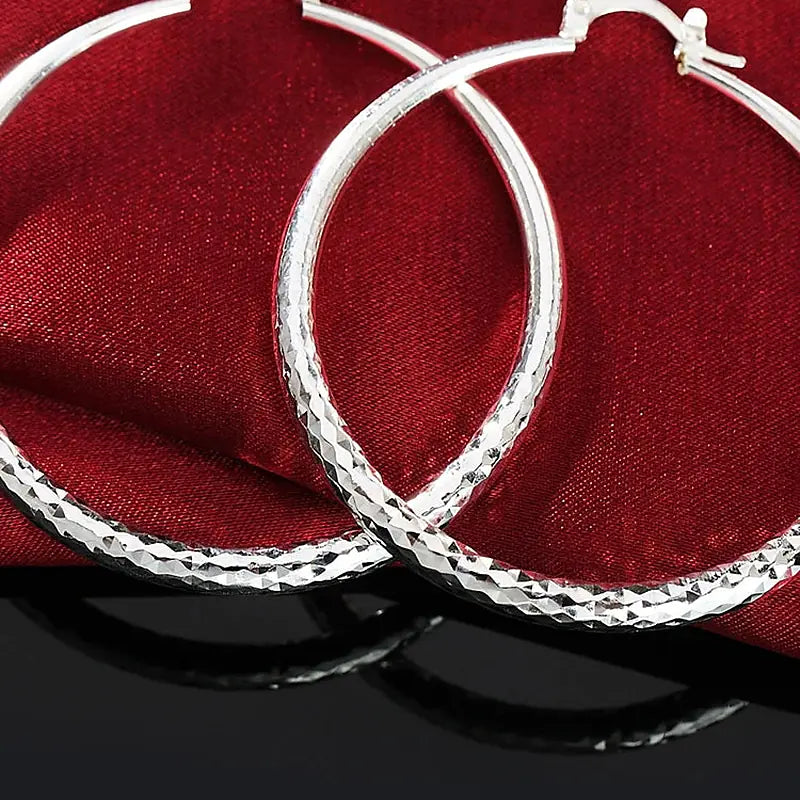 Boucles d'oreilles créoles Séraphine, la paire posée sur une soie rouge