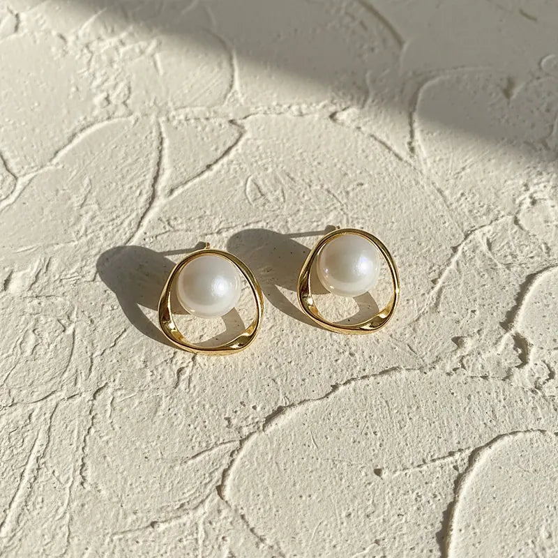 Boucles d'oreilles perles et anneau ondulé doré posées sur une surface en plâtre crème