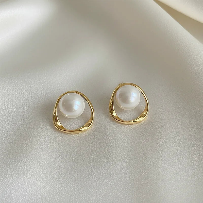 Boucles d'oreilles perles et anneau ondulé doré posées sur une soie ivoire