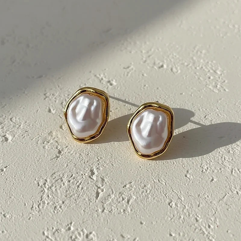 Boucles d'oreilles perles baroques dorées posées sur une surface en plâtre crème