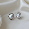 Boucles d'oreilles perles baroques argentées posées sur une soie ivoire