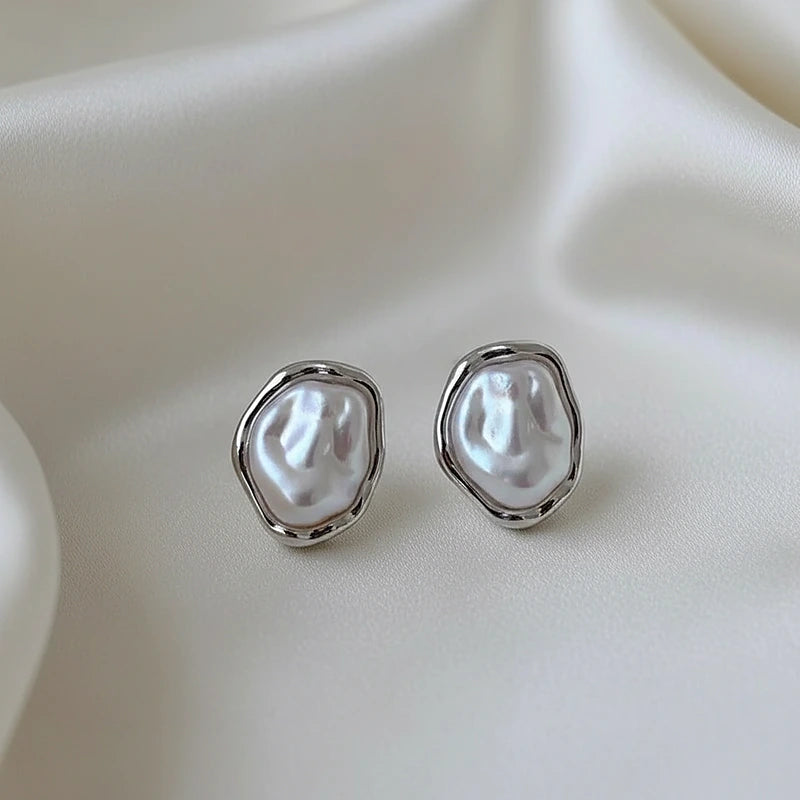Boucles d'oreilles perles baroques argentées posées sur une soie ivoire